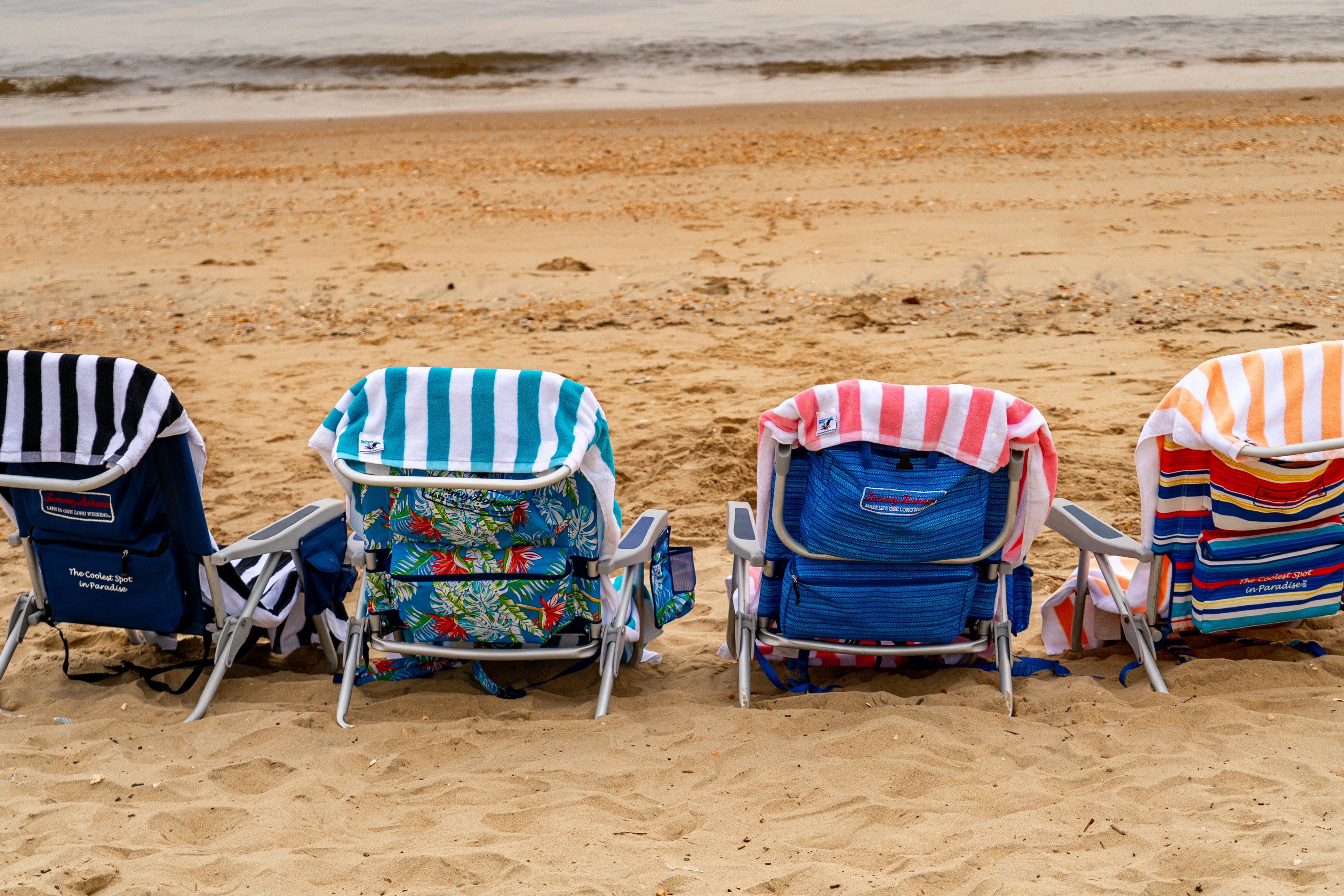 Four colorful beach chairs on a sandy beach with ocean in the background